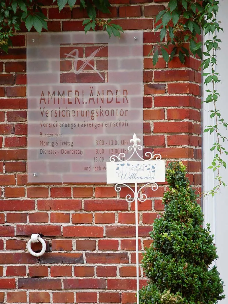 Schild des Ammerländer Versicherungskontors an der Backsteinfassade des Büros